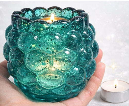 Teal bubble glass candle holder with a lit candle inside, held by a hand.