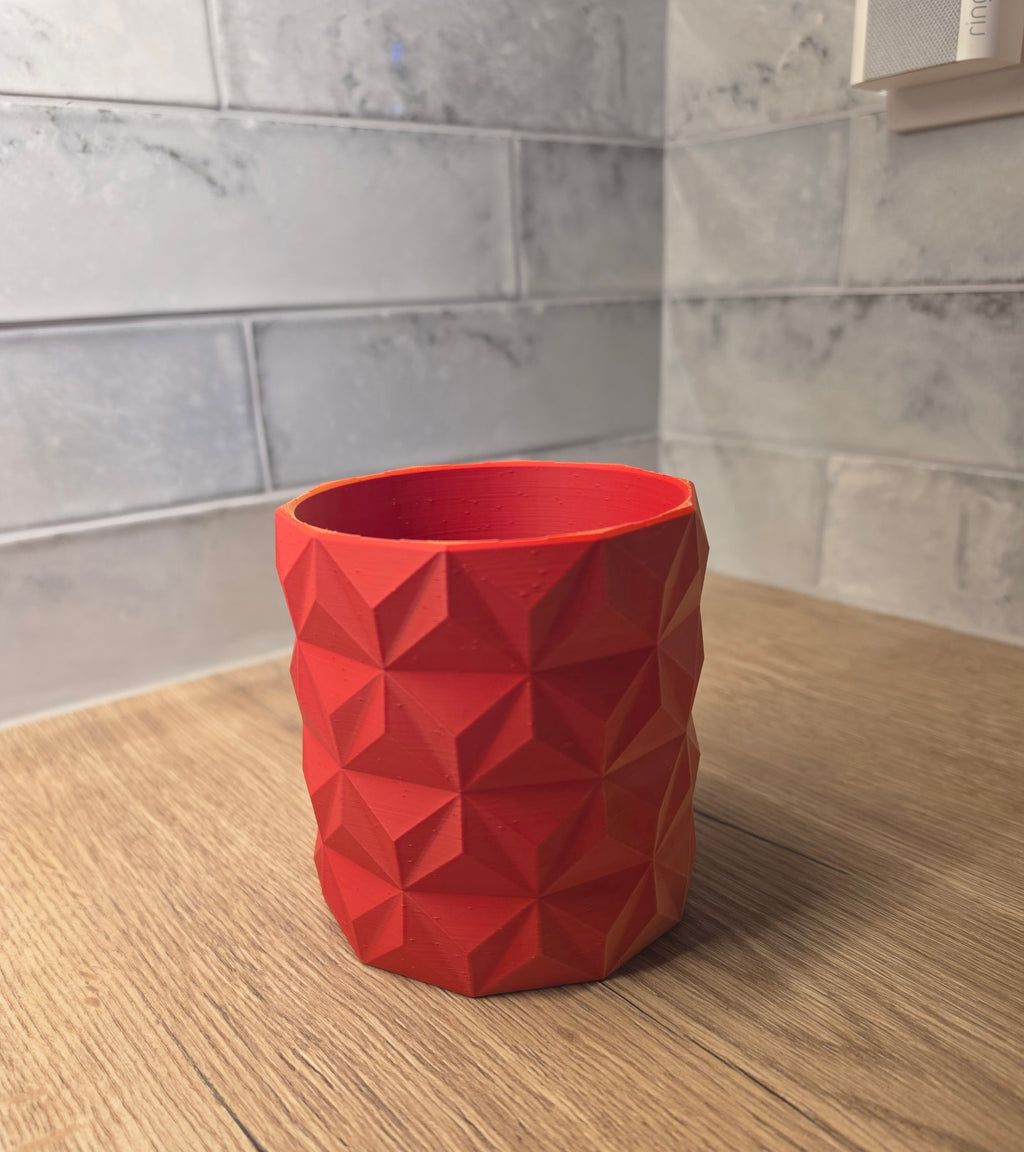 A red and yellow geometric faceted planter standing on a wooden surface against a grey tiled wall.