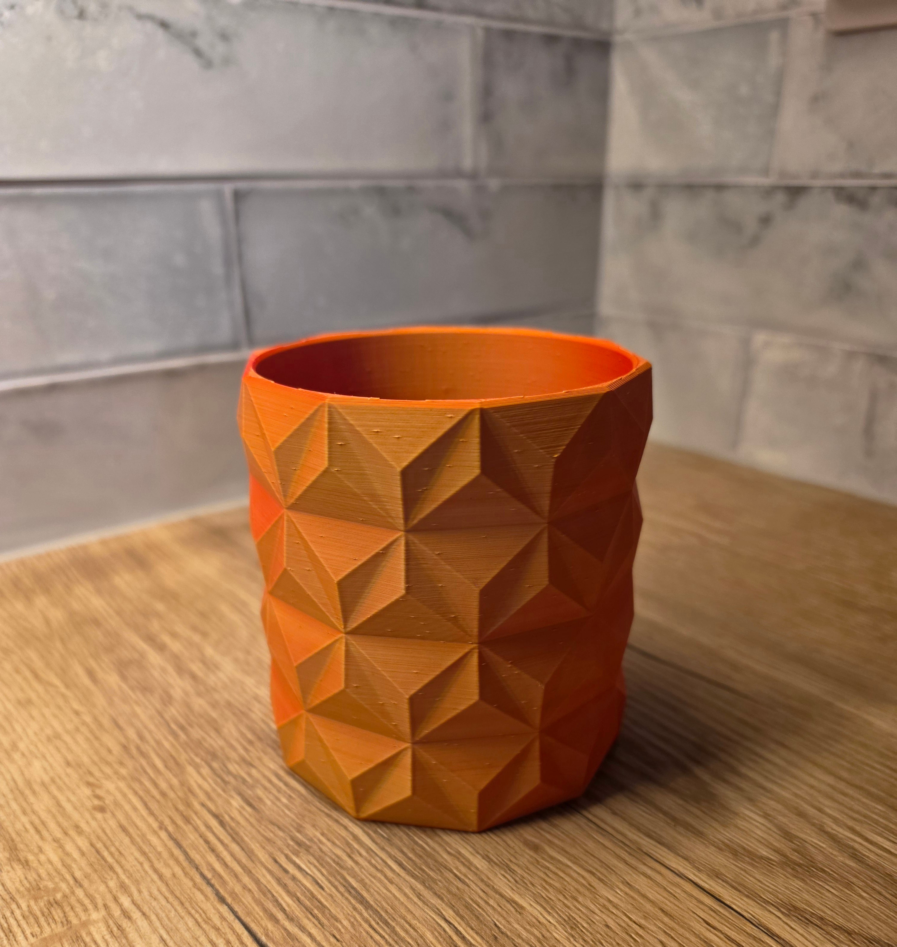 A red and yellow geometric faceted planter standing on a wooden surface against a grey tiled wall.