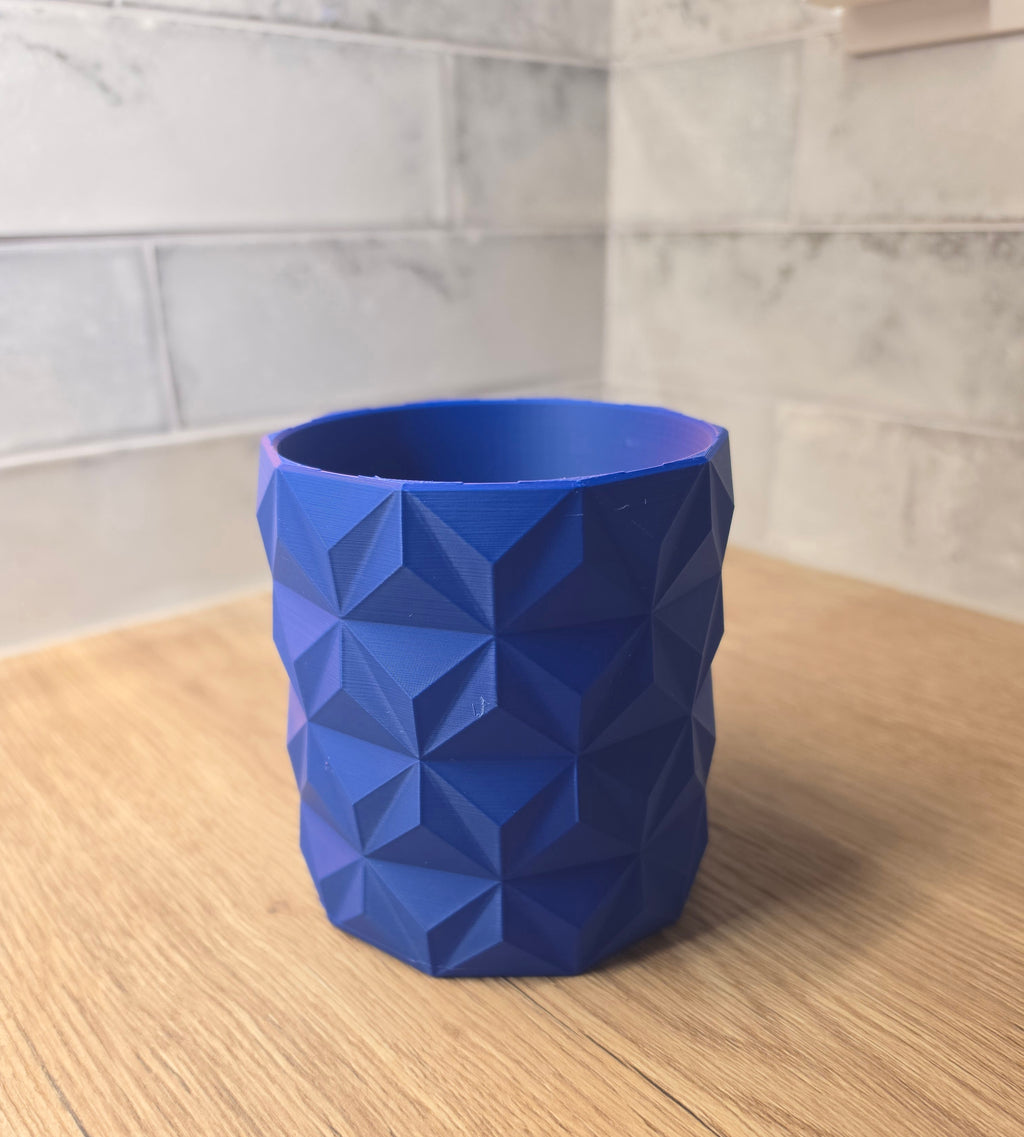 A Blue and Red  geometric faceted planter standing on a wooden surface against a grey tiled wall.