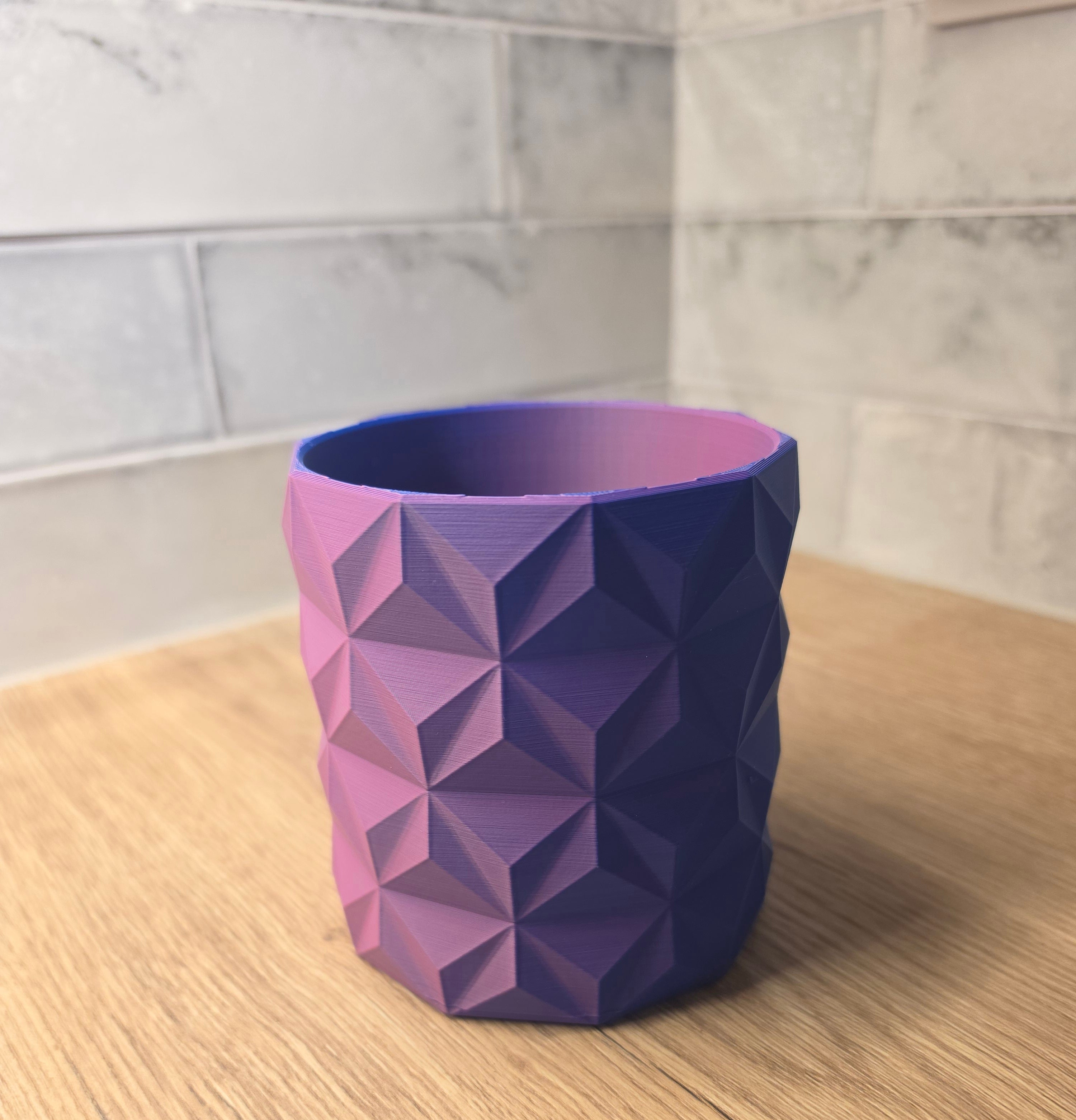 A Blue and Red  geometric faceted planter standing on a wooden surface against a grey tiled wall.