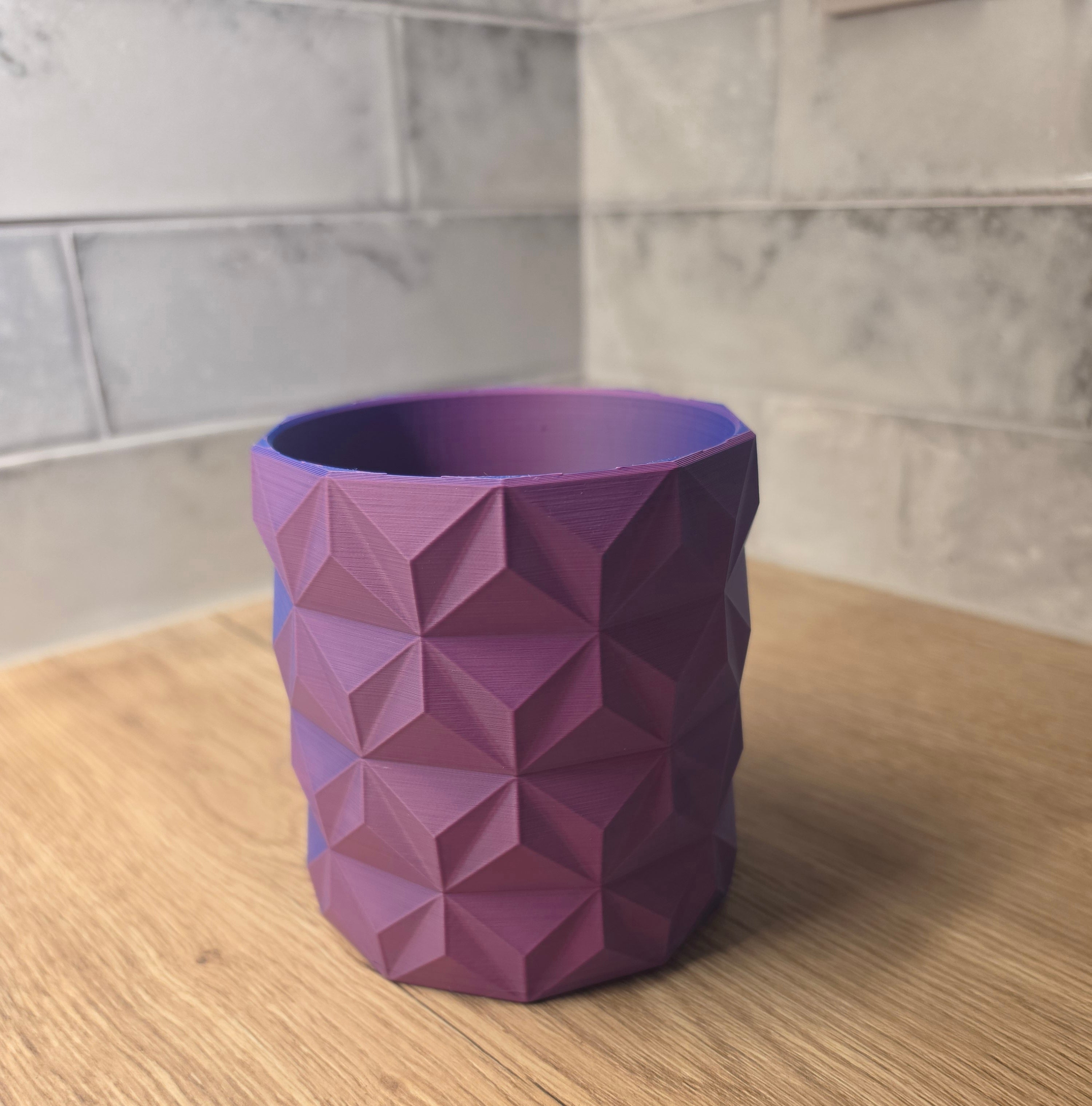 A Blue and Red  geometric faceted planter standing on a wooden surface against a grey tiled wall.