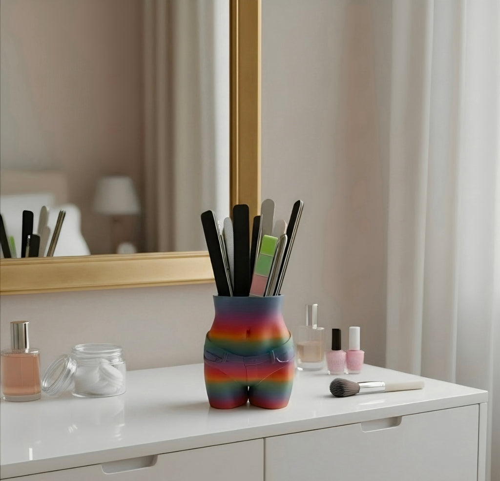 A novelty Pen Holder shaped like a rear silhouette, decorated with a vibrant rainbow gradient, holding nail tools and pens on a white vanity table in front of a mirror.