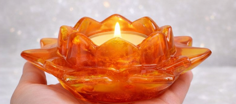 Orange Resin lotus flower candle holder with a lit candle inside, held by a hand against a blurred background.