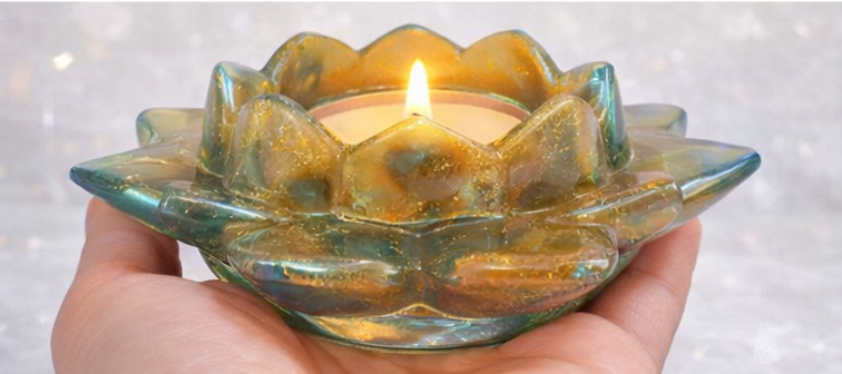 Hand holding a lit candle in a decorative Resin holder against a light background